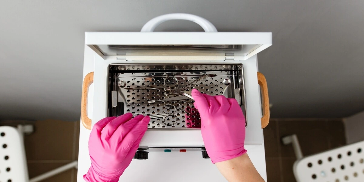 A pro in pink gloves placing tools in a sterilizer